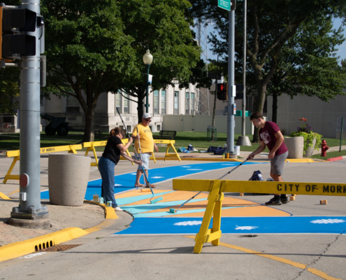 3 people painting bright colors onto pedestrian crosswalks in Morris, IL.